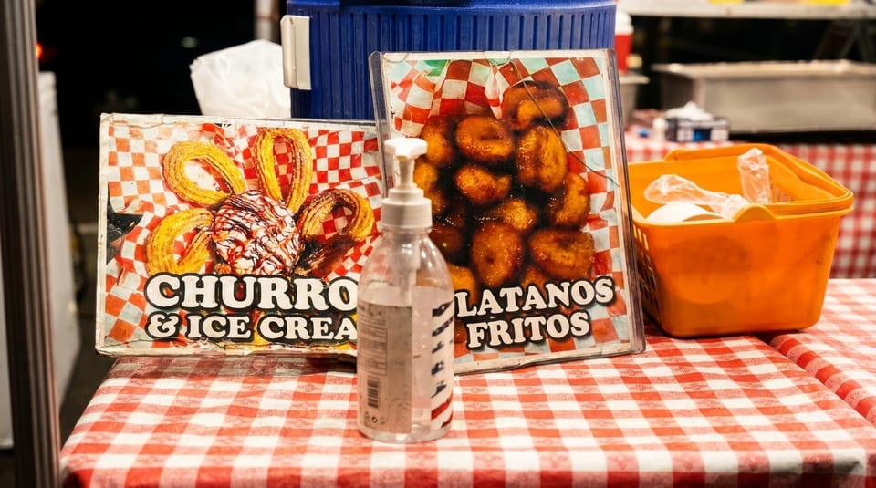 Two signs for churros and platanos fritos on a red and white checkered tablecloth.