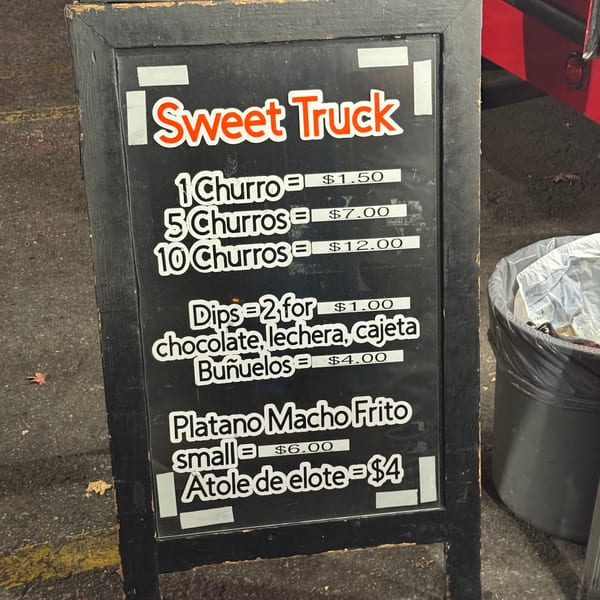A black chalkboard sign for "Sweet Truck" displays prices for churros, dips, buñuelos, and platano macho frito.