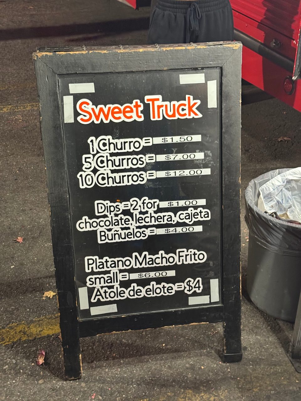 A black chalkboard sign for "Sweet Truck" displays prices for churros, dips, buñuelos, and platano macho frito.